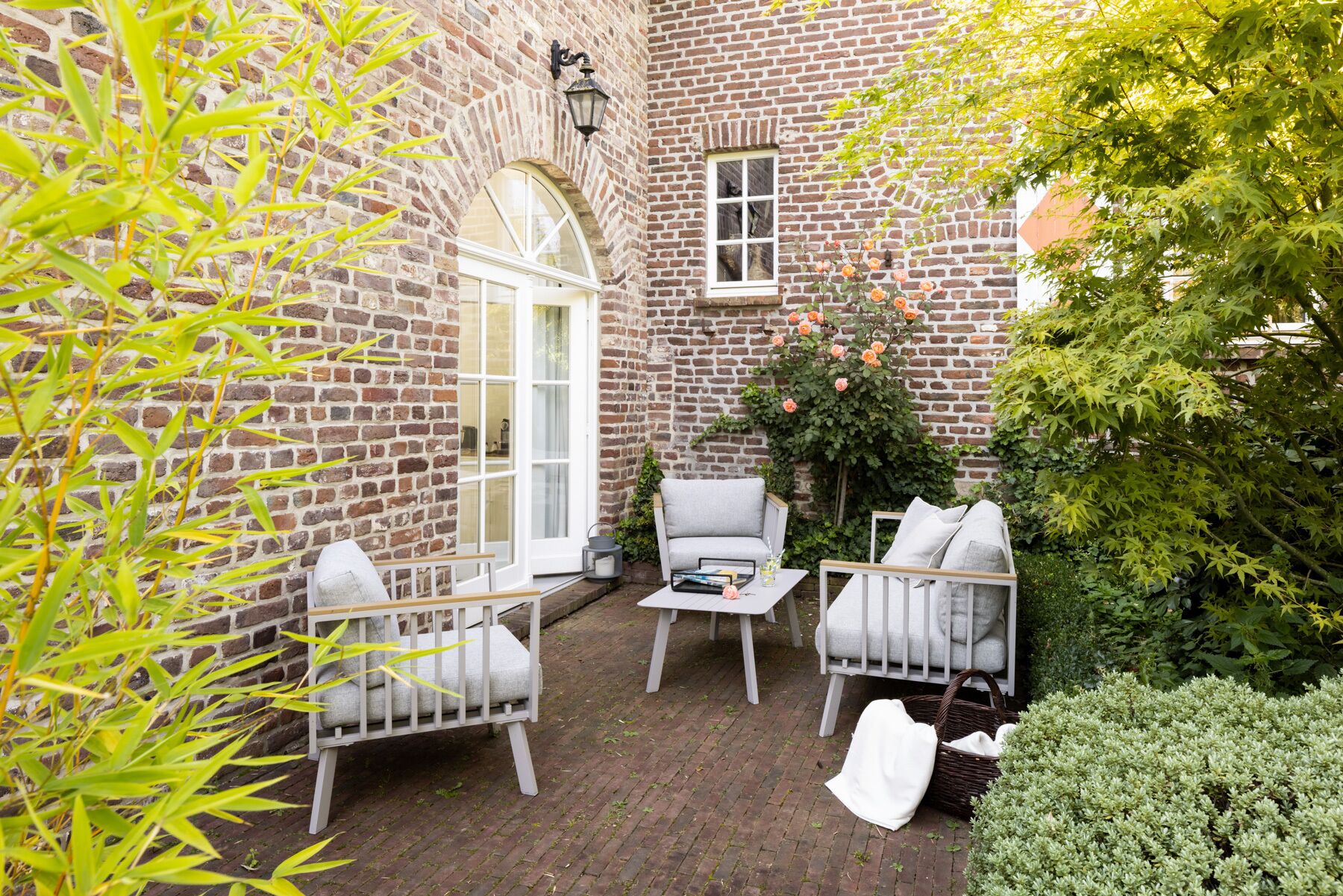 A brick courtyard with two white chairs, a small table, and a white bench.