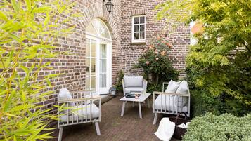 A brick courtyard with two white chairs, a small table, and a white bench.