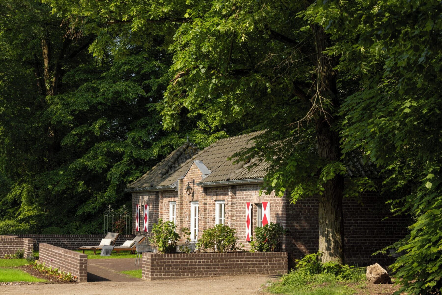 A brick building with a tiled roof, surrounded by dense green foliage.