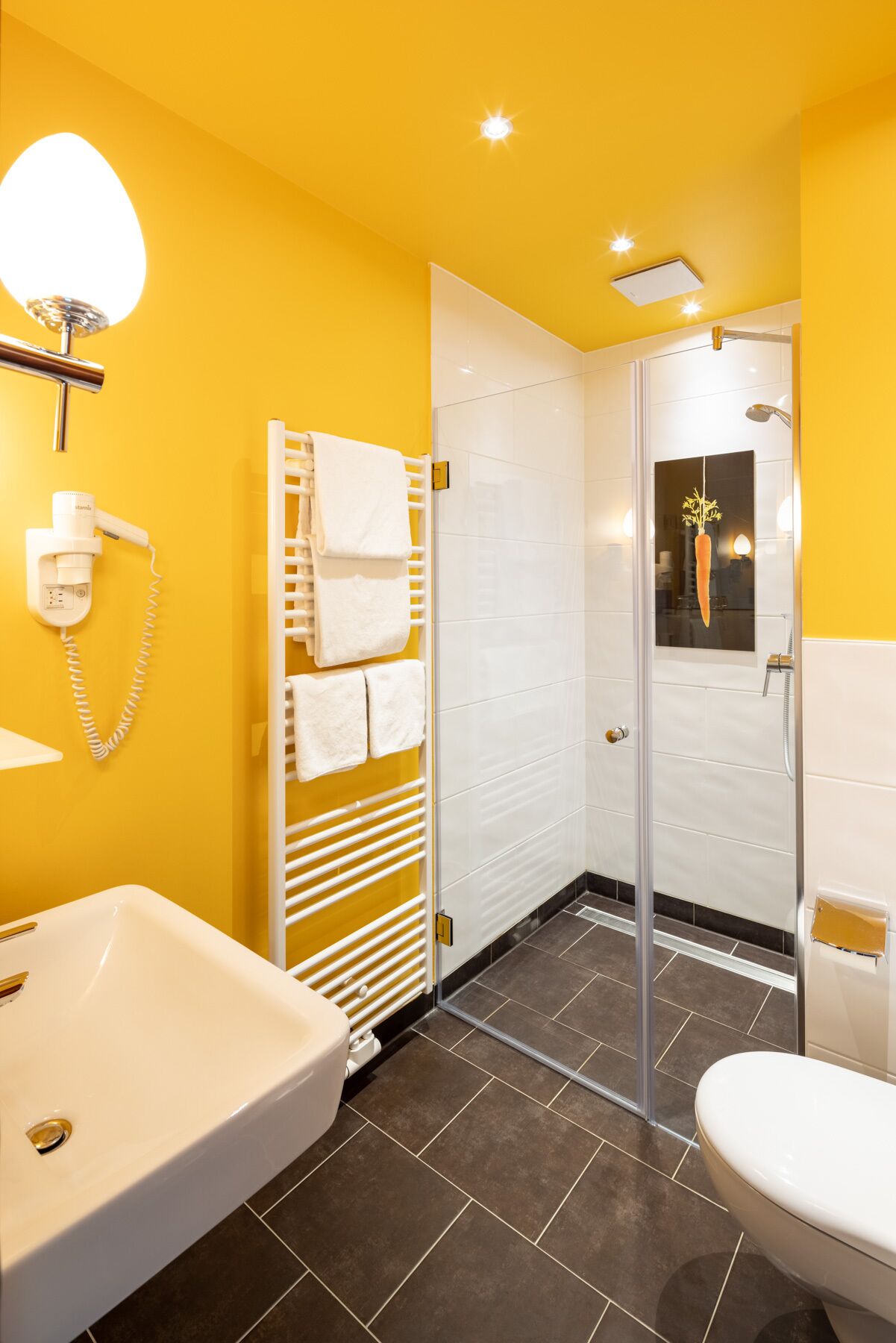 A bathroom with a white sink, a toilet, a glass shower enclosure, and a towel rack with multiple towels.
