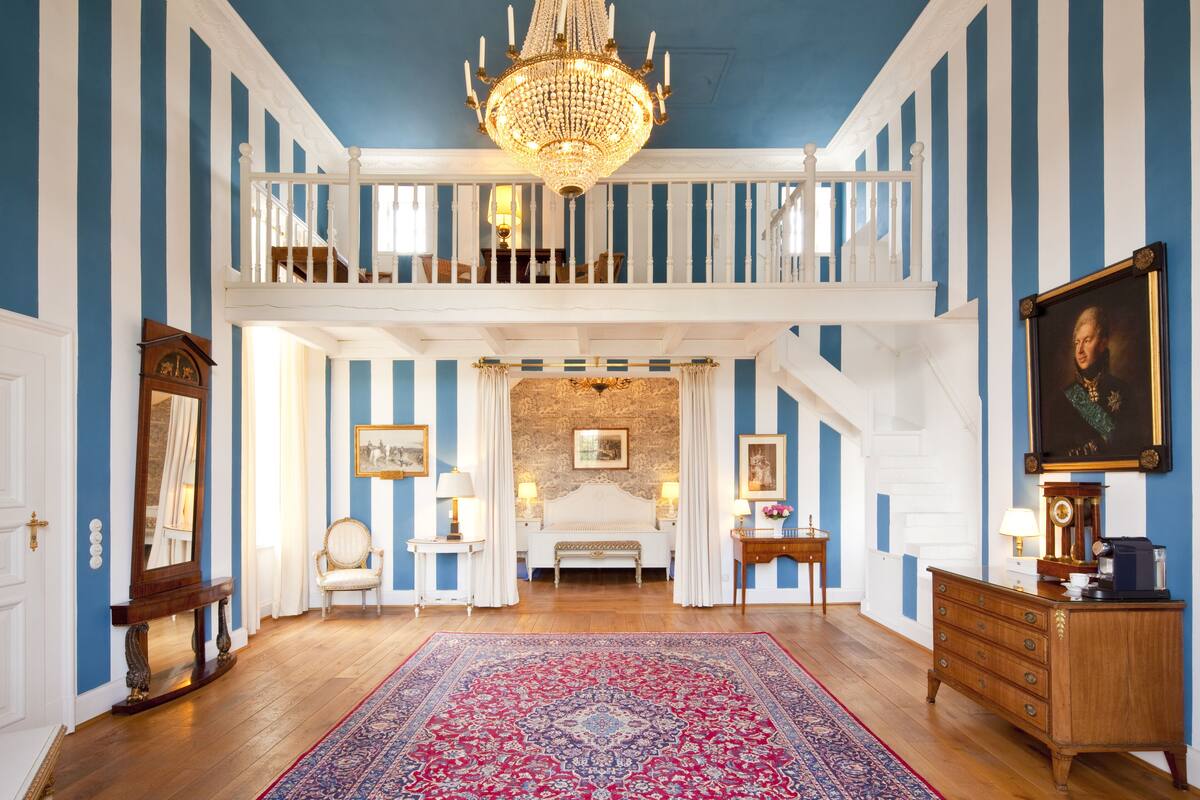 Una habitación amplia con una cama grande, un candelabro, una escalera y un cuadro en la pared.