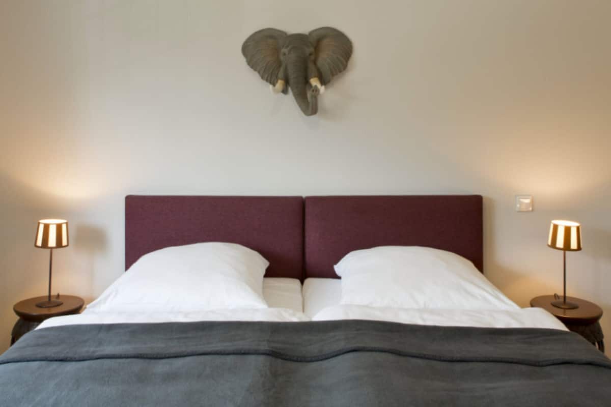 Una cama con cabecera, dos lámparas de noche y una escultura de elefante en la pared.