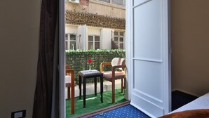 Habitació amb vista a un edifici amb façana decorativa, una taula petita amb un ram i una cadira.