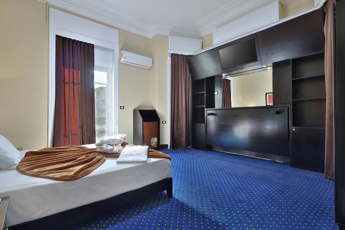 A hotel room with a bed, a TV, a wardrobe, and a window with curtains.