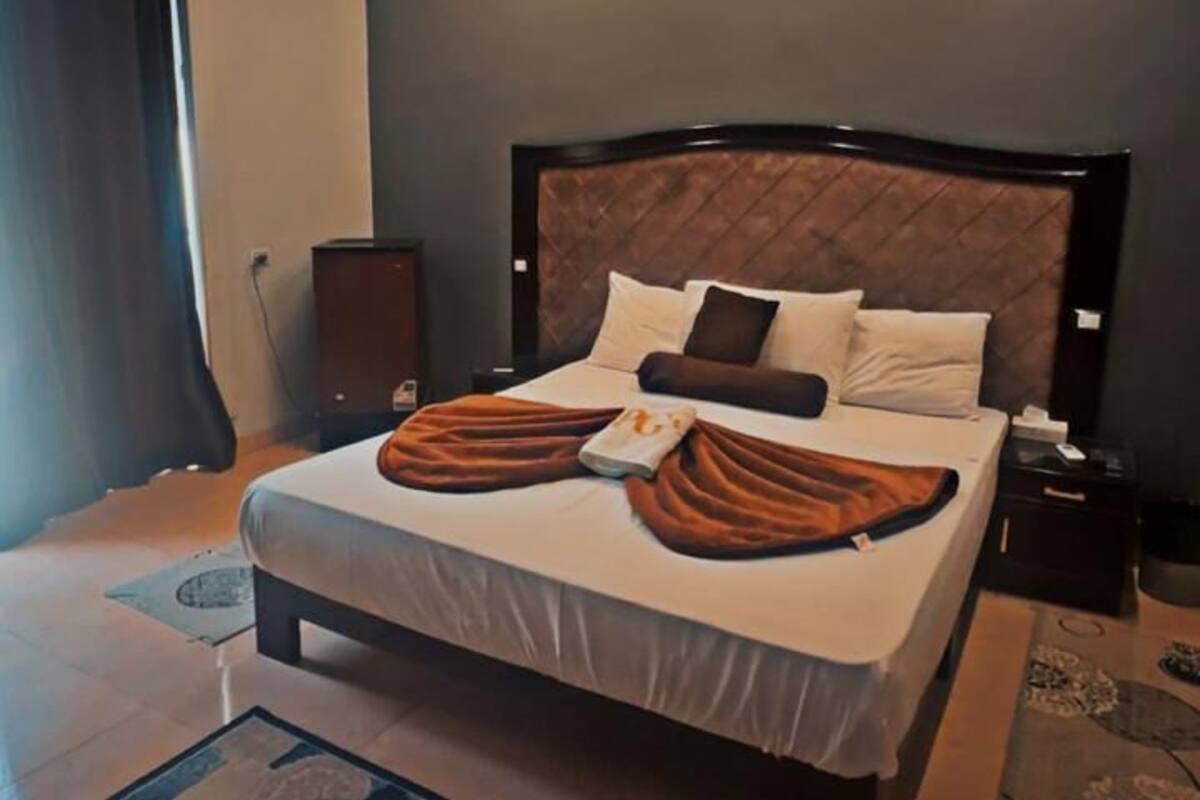 A modern hotel room with a large bed, a bedside table, a nightstand, and a patterned rug.