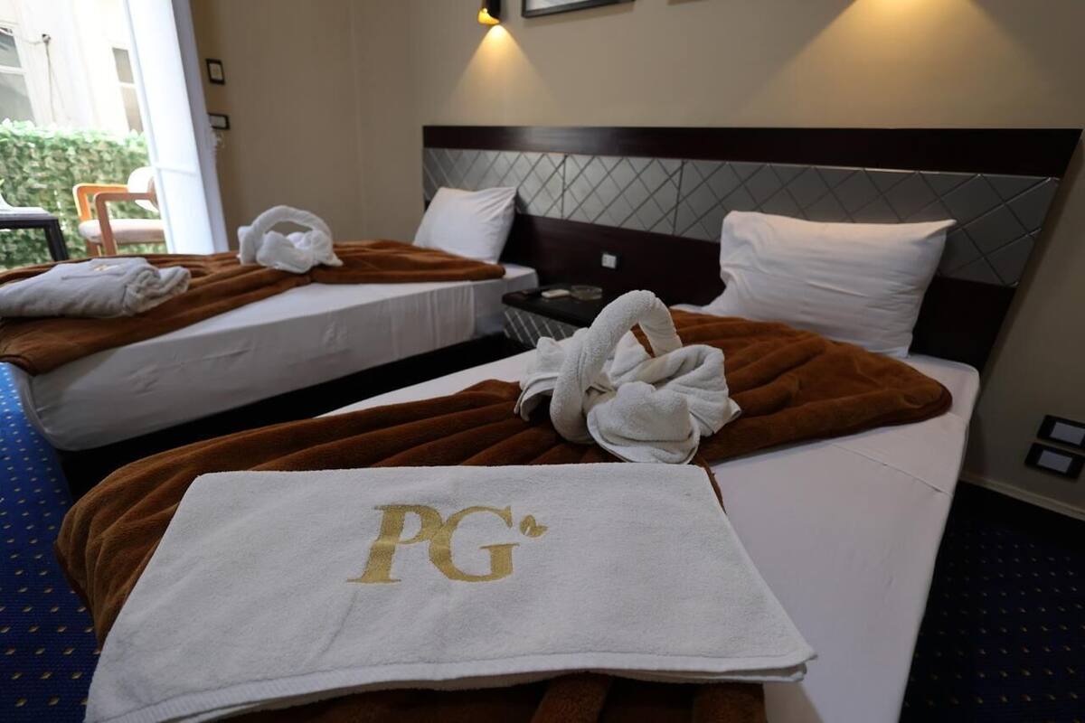 A hotel room with two beds, each with a brown blanket and white pillows. There is a towel with 'PG' on it on the floor.