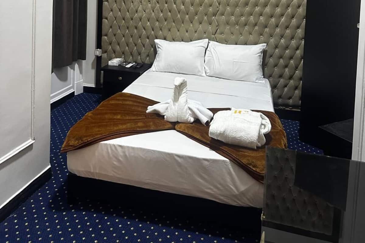 A hotel room with a large bed, a headboard, a bedside table, an air conditioning unit, and a window with curtains.
