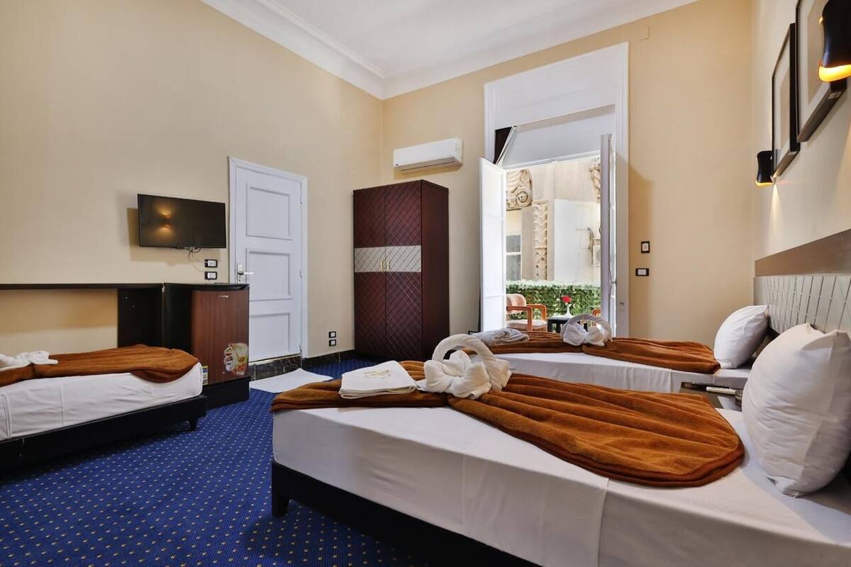 A hotel room with two beds, a TV, a wardrobe, and a bathroom visible through an open door.