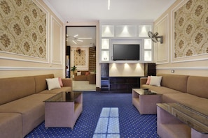 A hotel room with a sofa, coffee table, TV, fireplace, and patterned wallpaper. - Cairo Paradise Hotel (Cairo)