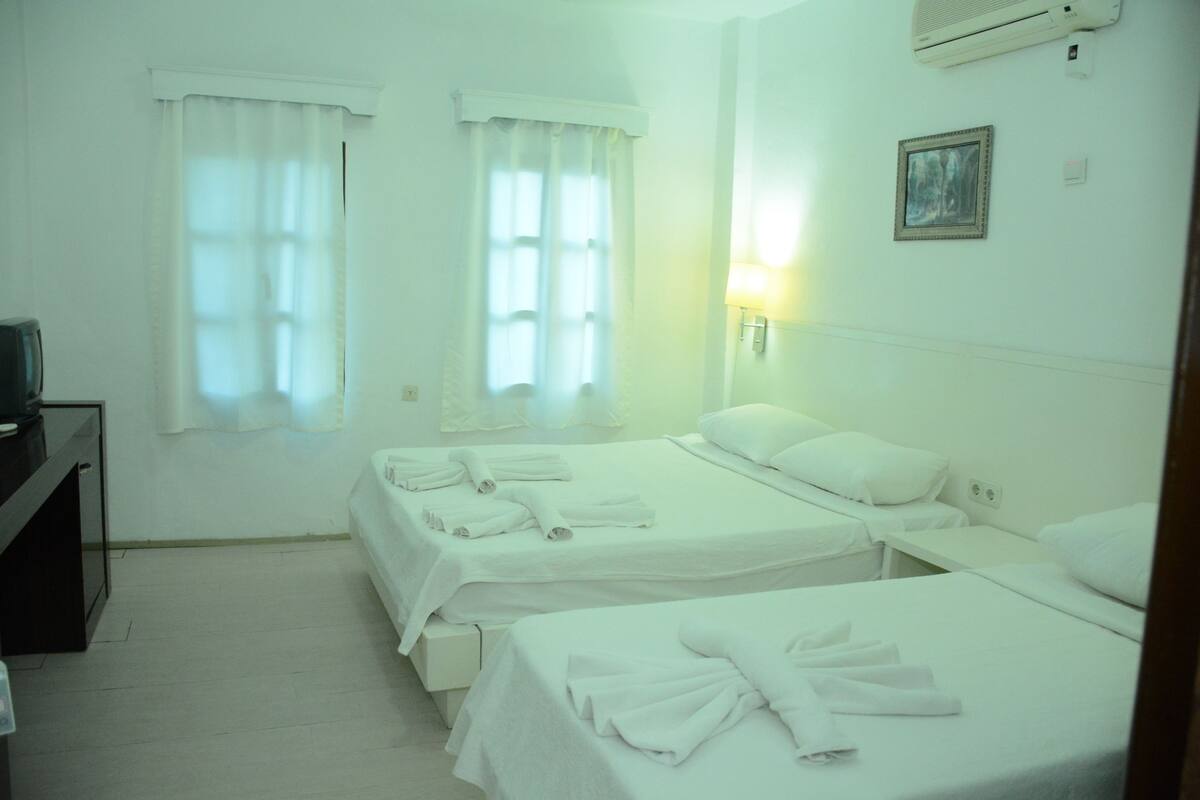 A hotel room with two beds, white bedding, a TV on a stand, and a wall-mounted air conditioner.
