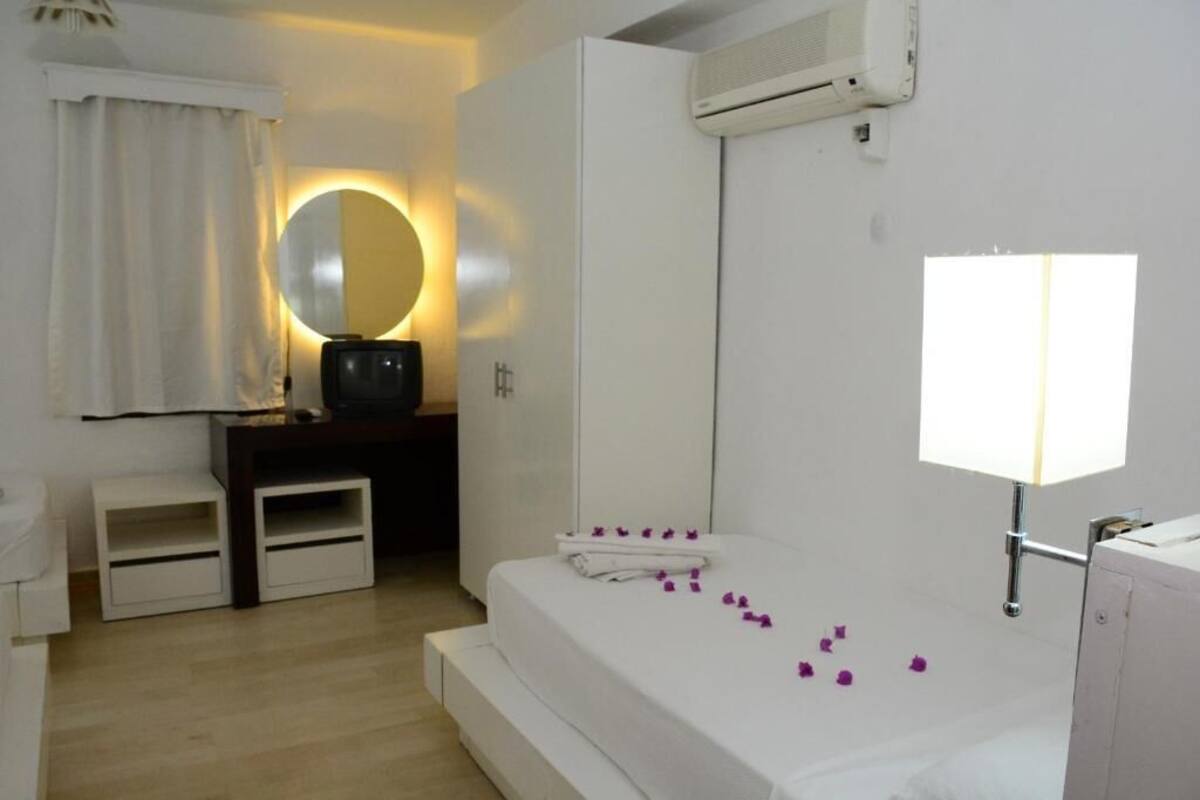 A hotel room with a bed, a bedside table, a mirror, an air conditioning unit, and a window.