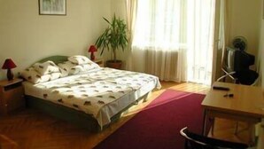 Una camera da letto con un letto, una scrivania, una sedia, una lampada, una pianta e una finestra con tende.