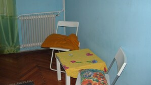 Una stanza piccola con un termosifone, una sedia bianca e un tavolo con tovaglia floreale.