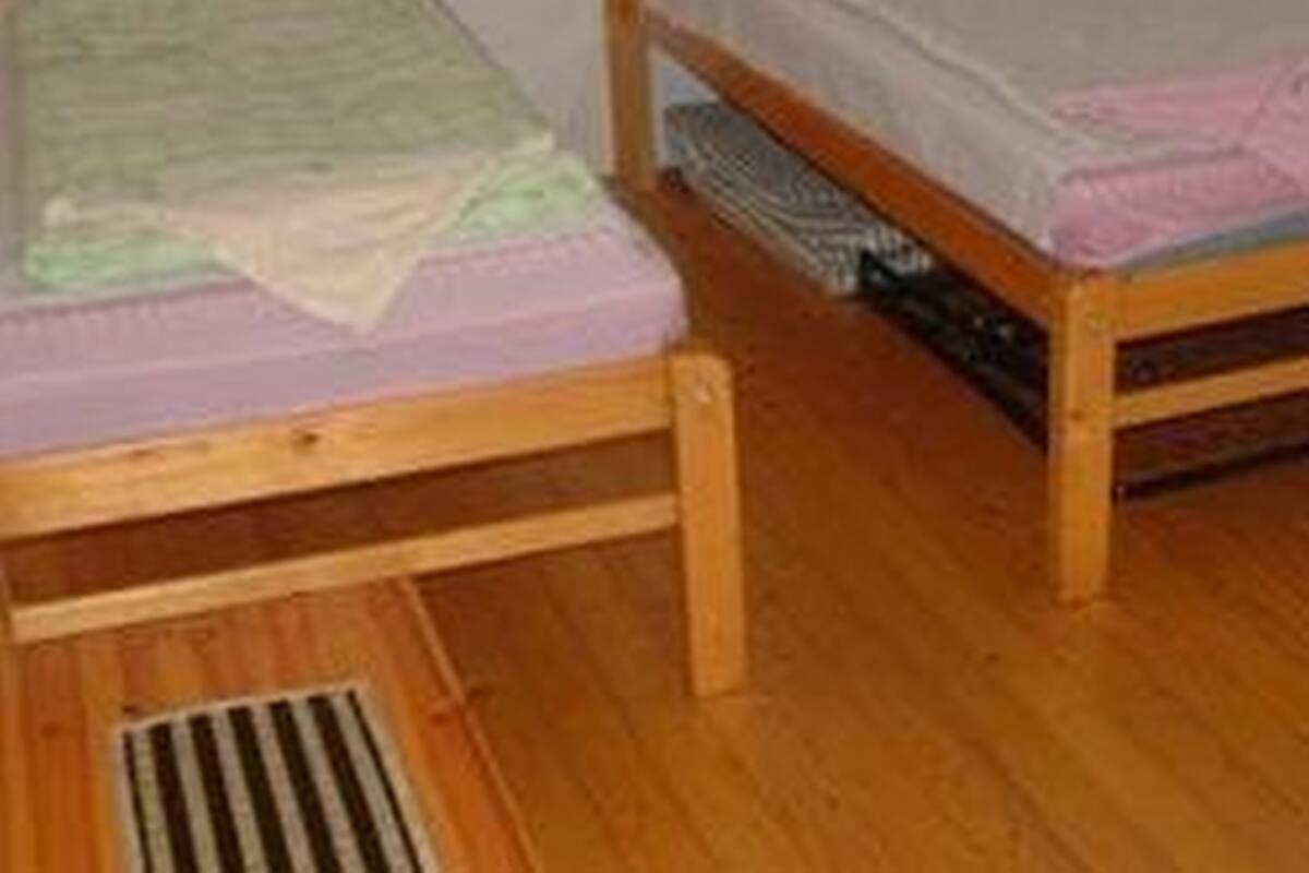 A small, single-bed room with wooden flooring and a simple, unadorned design.