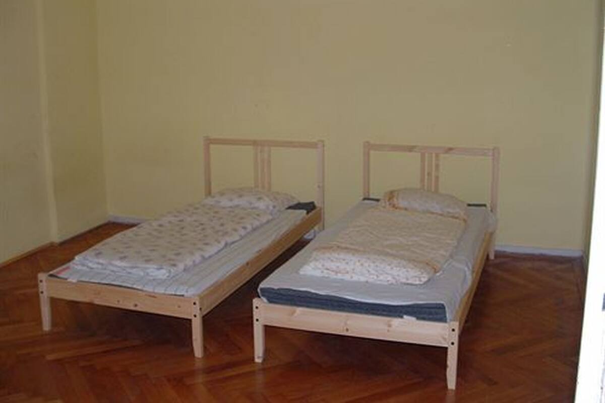 Two wooden single beds with headboards, a wooden floor, and a plain yellow wall.
