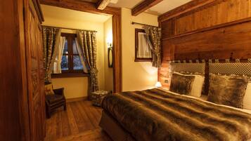A cozy bedroom with a wooden headboard, a large bed with a dark blanket, a small chair, and a window with curtains.