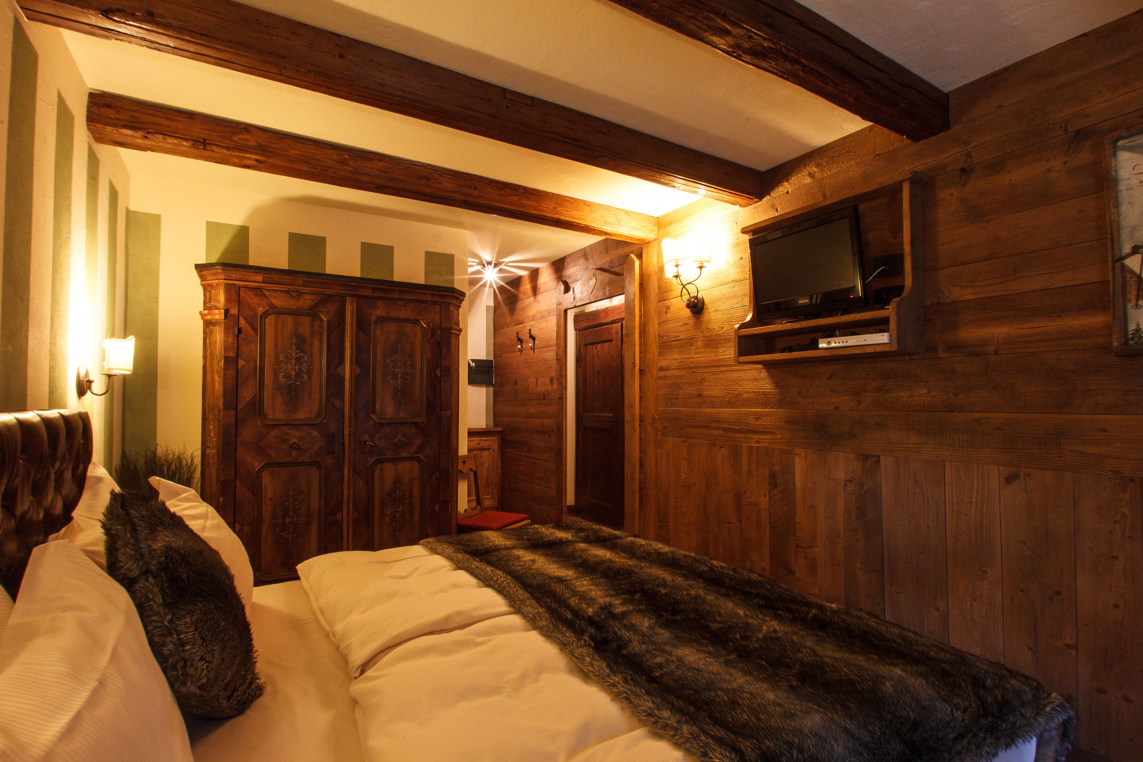 A wooden-paneled room with a bed, a television mounted on the wall, and a wooden wardrobe.