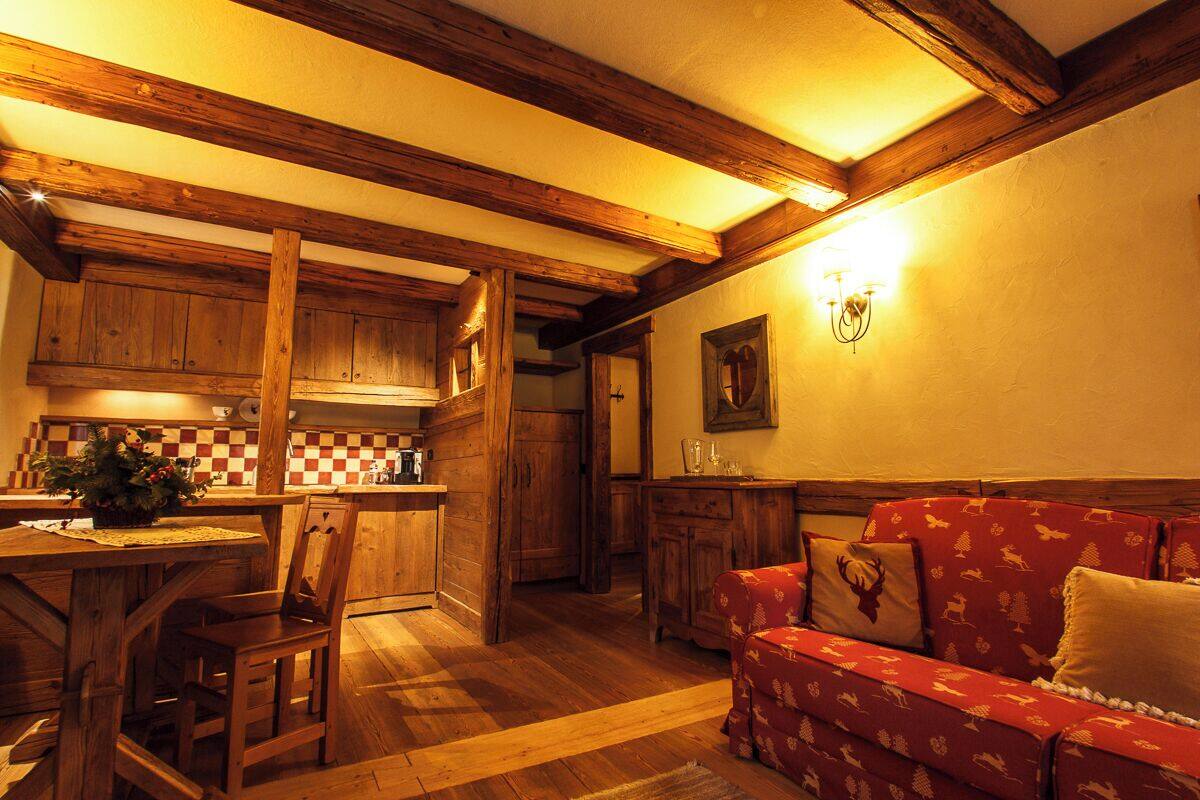 Un interior acogedor con vigas de madera, un salpicadero a cuadros, un sofá rojo estampado y una zona de comedor con mesa y sillas de madera.