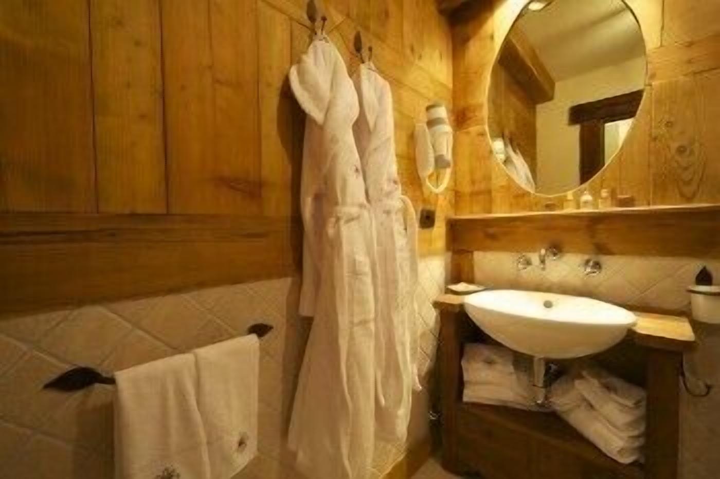 A wooden bathroom with a sink, mirror, and hanging robes.