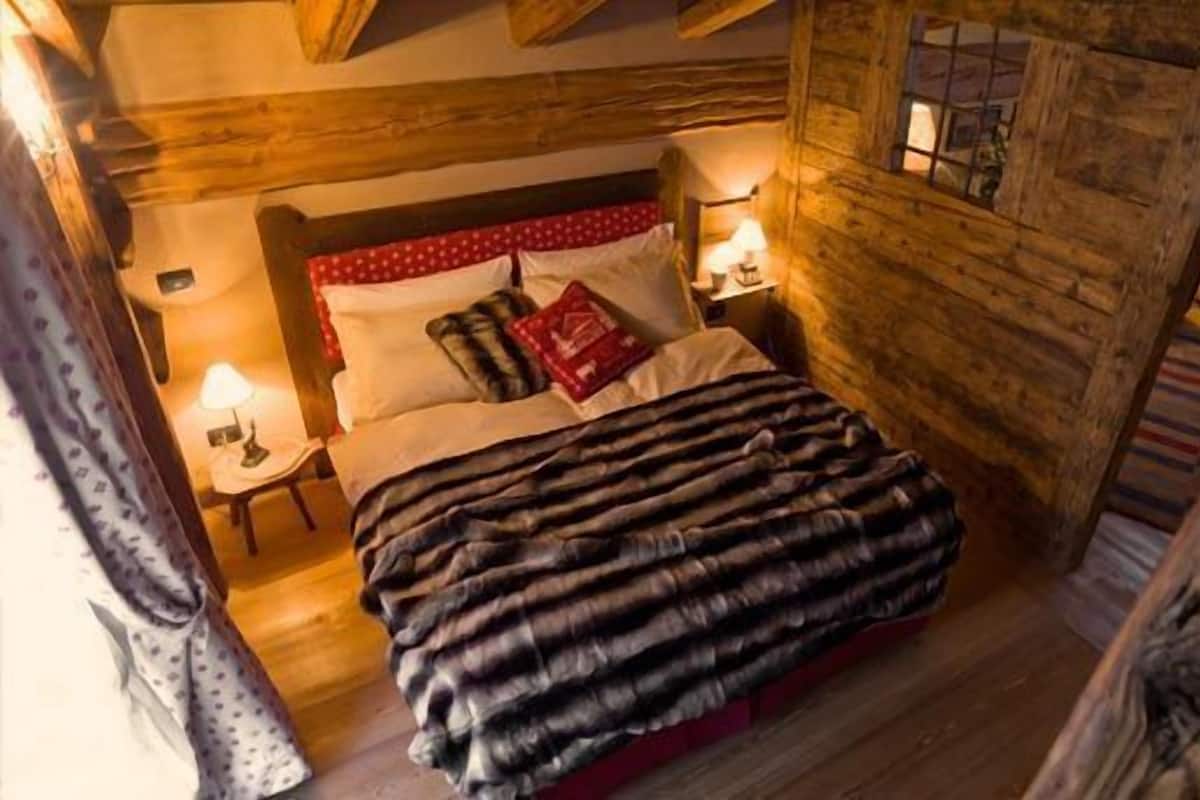 Una habitación acogedora de madera con una cama, dos mesitas de noche y un ventanal.