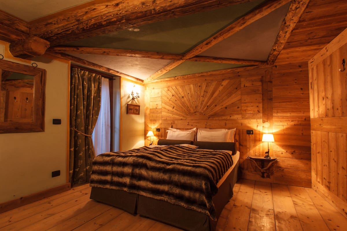 Una habitación de madera con una cama, dos lámparas de noche y una ventana con cortinas.
