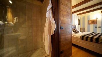 A room with a wooden ceiling, a bed with a striped blanket, and a glass shower enclosure.