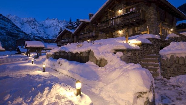Een met sneeuw bedekte lodge met stenen muren en houten balkons, verlicht door sfeerverlichting.