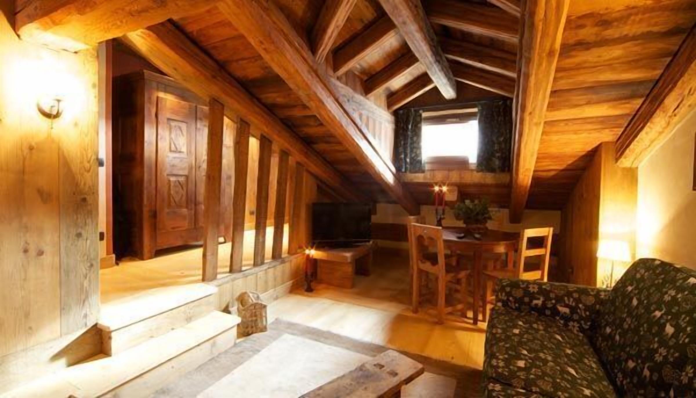 Ein gemütliches Dachzimmer mit Holzbalken, einem Bett, einem Tisch und einem Fernseher.