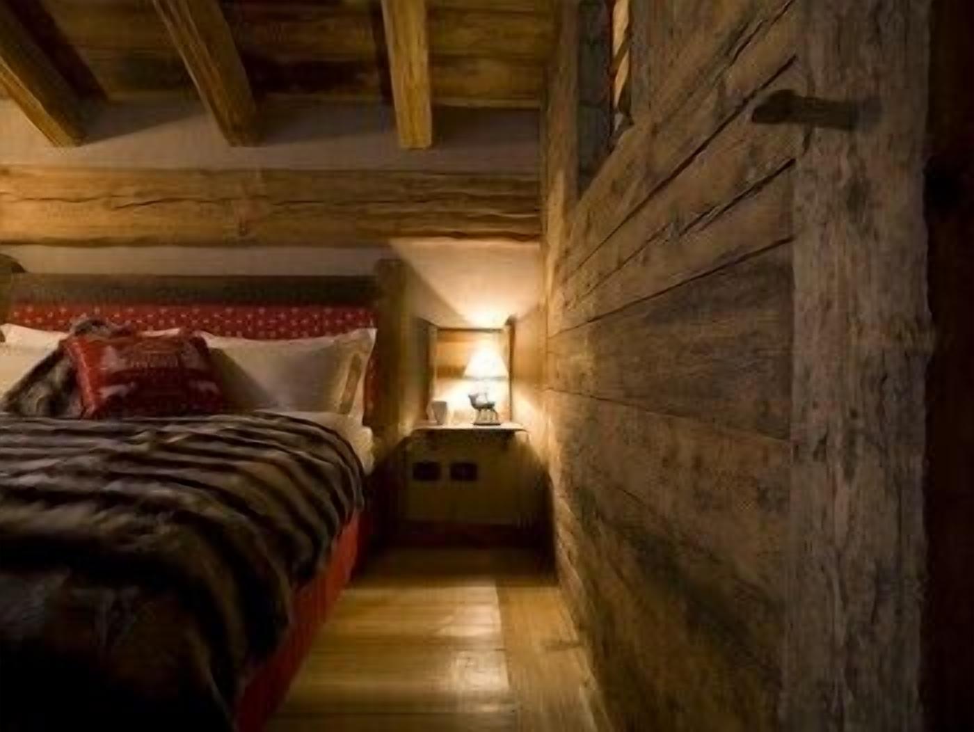 Une pièce étroite au plancher de bois, comprenant un lit, une table de chevet et une lampe.