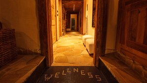 Een hal met stenen vloer die leidt naar een wellnessruimte, met houten deuren en een welkomstmat waarop 