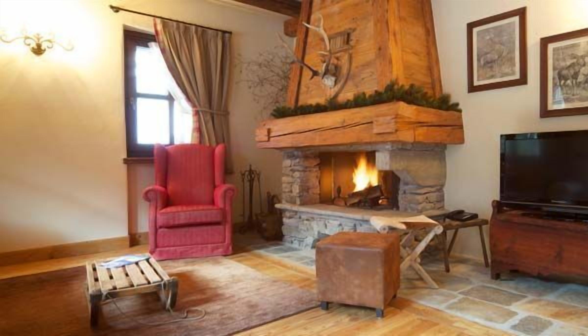 A cozy living room with a stone fireplace, a red armchair, a wooden coffee table, and a television.