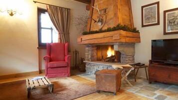 A cozy living room with a stone fireplace, a red armchair, a wooden coffee table, and a television.