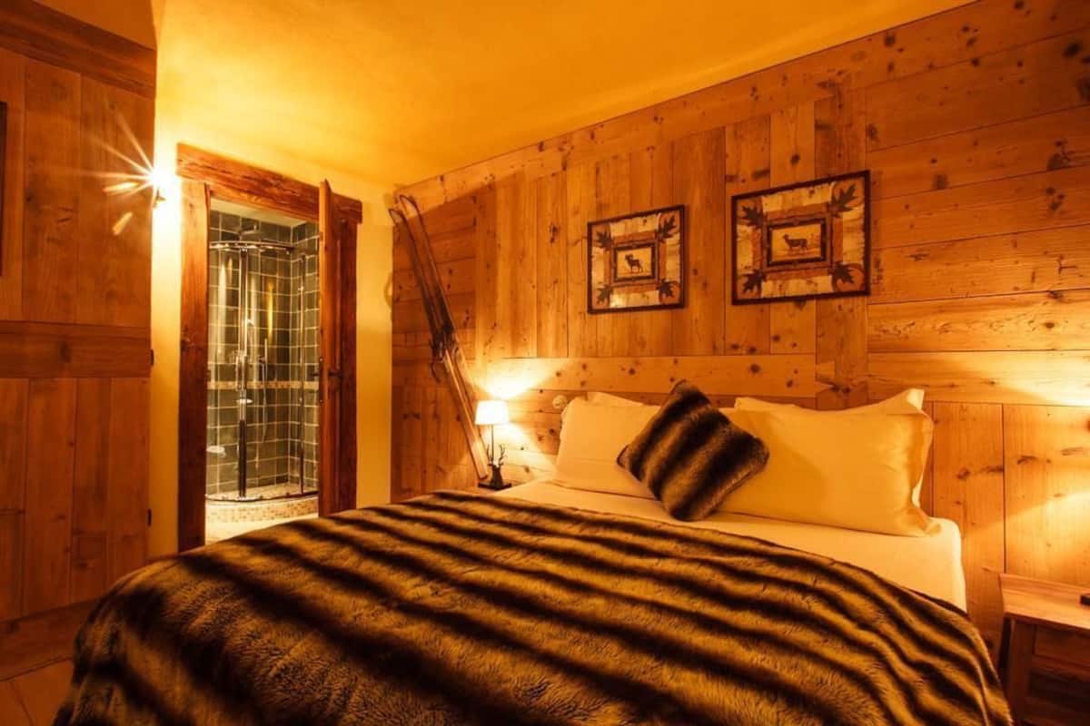 Dormitorio de cabaña de madera con cama, mesita de noche, lámpara y zona de ducha.