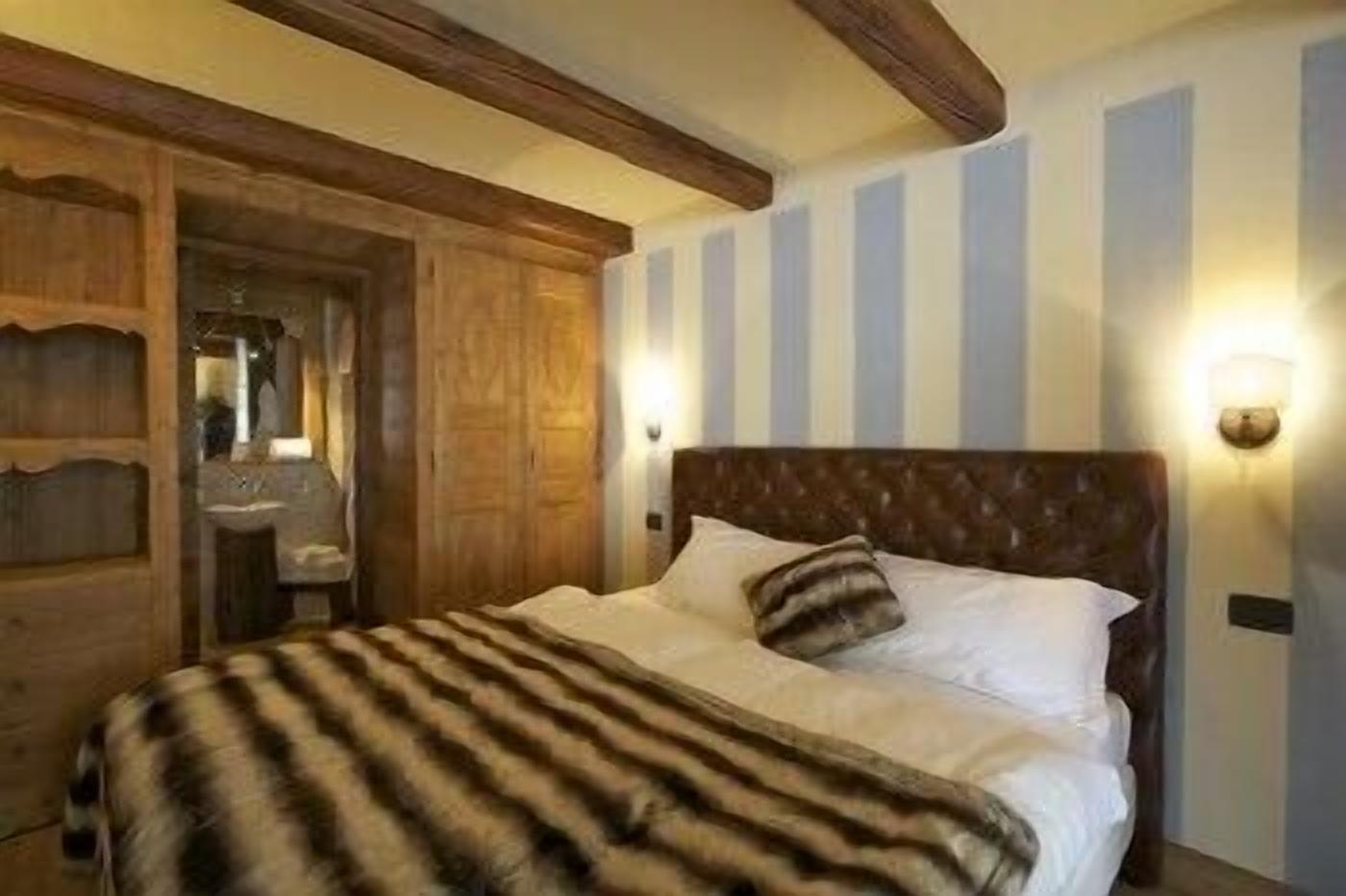 A bedroom with a large bed, wooden headboard, striped wall, and a wooden wardrobe.