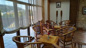 A dining area with wooden furniture, a table with a vase, and a view through large windows. - Hotel Rustico Prado Da Viña (Fisterra)