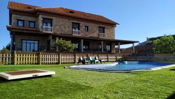 Una casa de piedra de dos pisos con piscina, patio cercado y terraza de madera.
