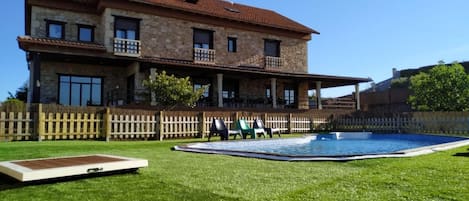 A two-story stone house with a swimming pool, a fenced yard, and a wooden deck.