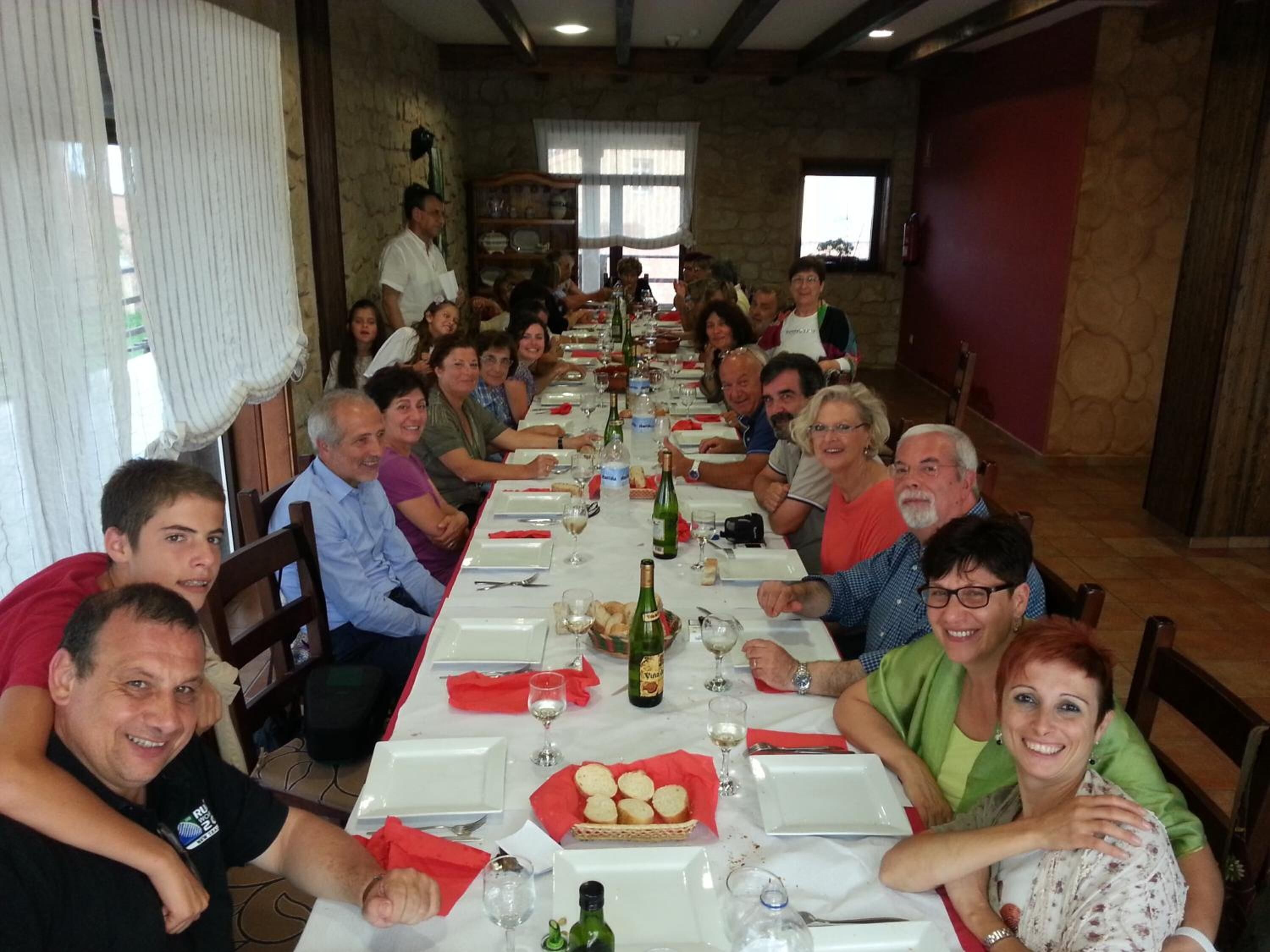 Una llarga taula de dinar preparada per a les menjades, amb diverses persones assegudes al voltant.