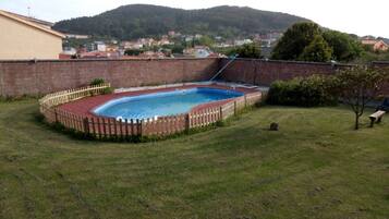 Un patio trasero con piscina rodeada por una cerca de madera, césped y un muro de ladrillo.