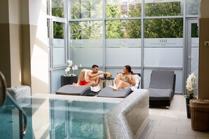 A poolside area with lounge chairs, a hot tub, and a glass-enclosed pool.