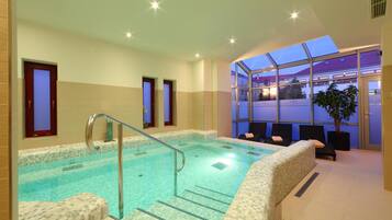 Una piscina interior con agua cristalina, suelo de baldosas y cerramiento de vidrio con asientos.
