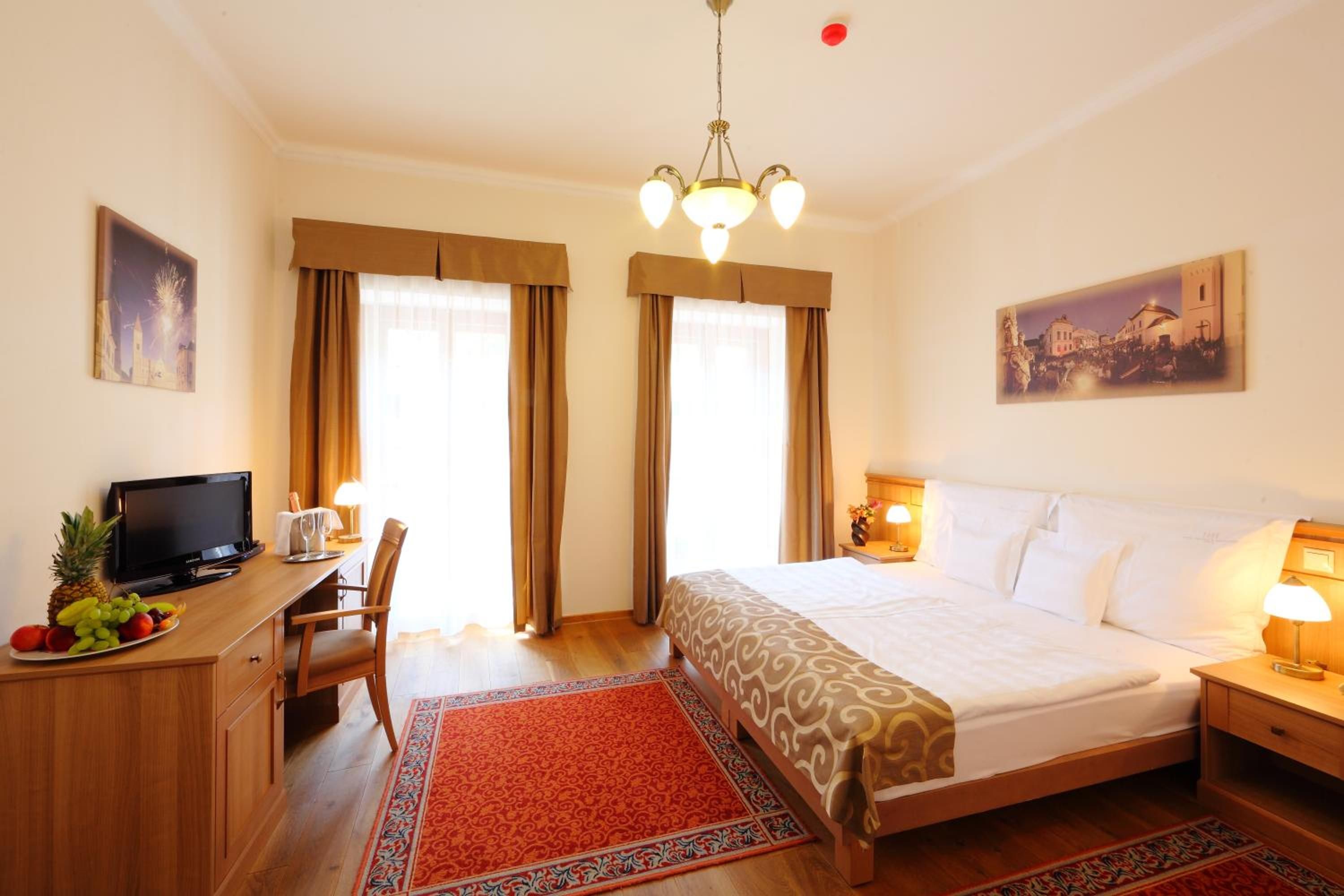 A hotel room with a bed, desk, television, and artwork on the walls.