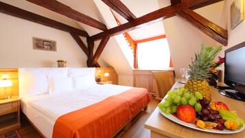 Quarto de hotel com cama, secretária com mesa de frutas, televisão e vigas de madeira no teto.