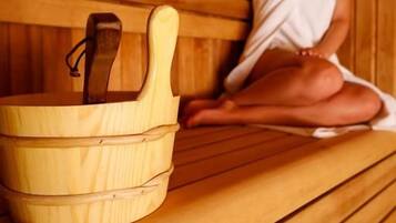 A person sitting in a wooden sauna with a wooden bucket.