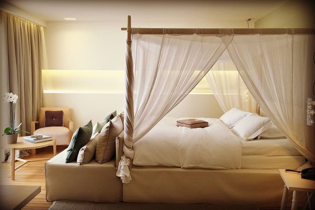 A bedroom with a four-poster canopy bed, a sofa, a small table, and a chair.