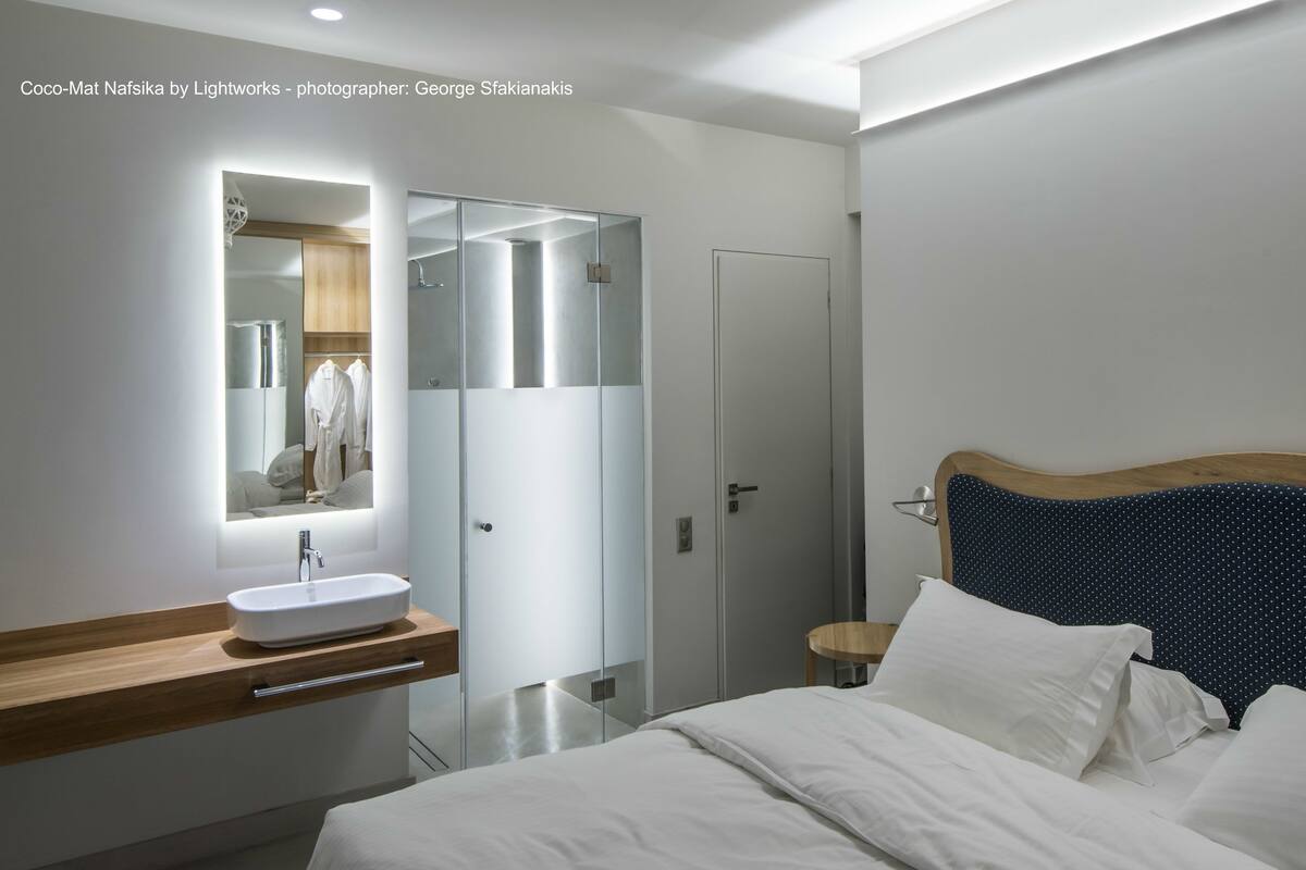 A modern hotel room with a wooden vanity, a large mirror, a bed with white linens, and a dark blue polka dot headboard.