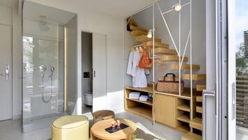 A modern bathroom with a glass-enclosed shower, a wooden vanity, and a seating area with a table and chair.