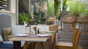 A dining area with a table set for two, a potted plant, and wicker chairs. - COCO-MAT Hotel Nafsika (Kifisia)