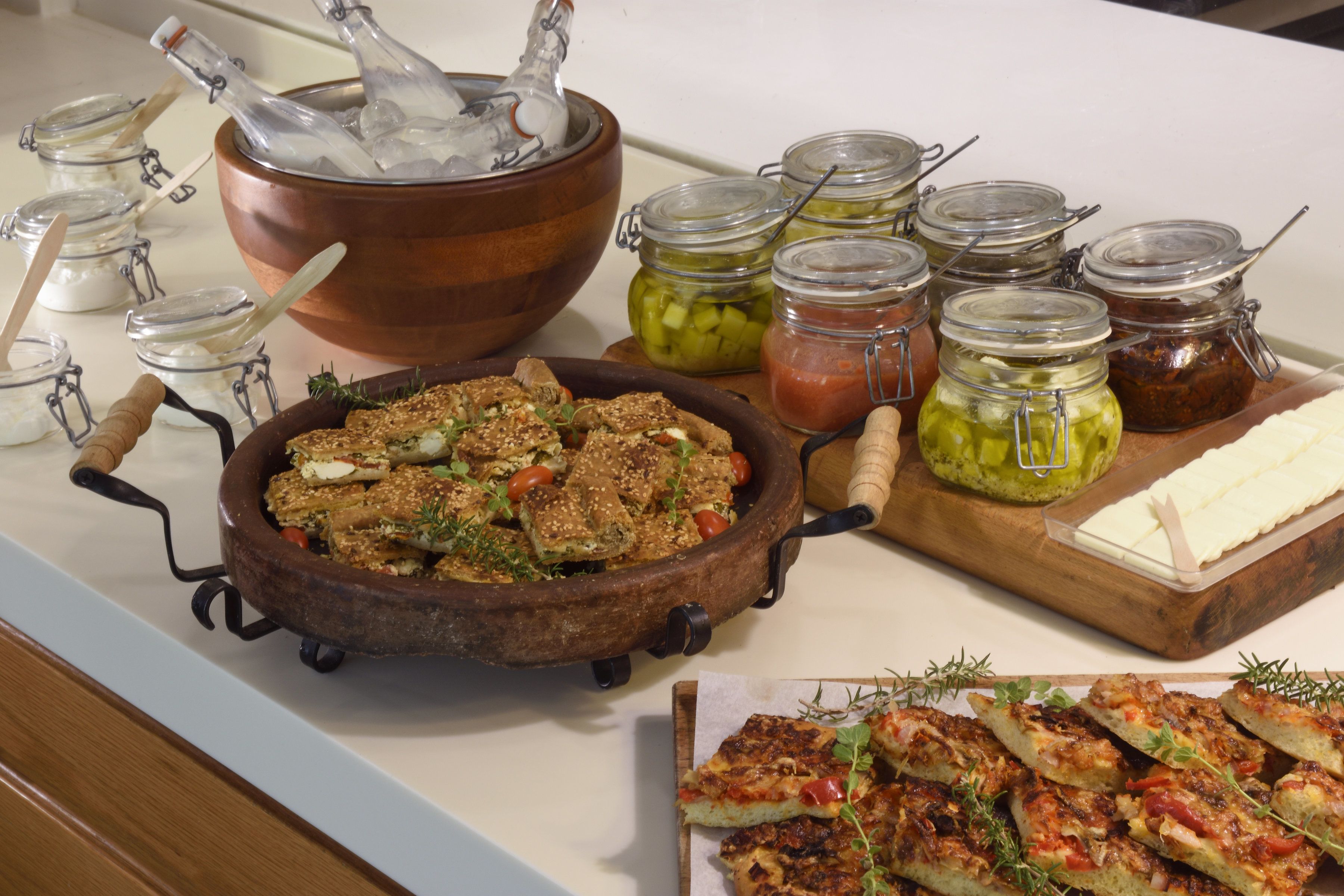 A buffet with various dishes, including a large pot, jars of pickles, and a wooden board with cheese.