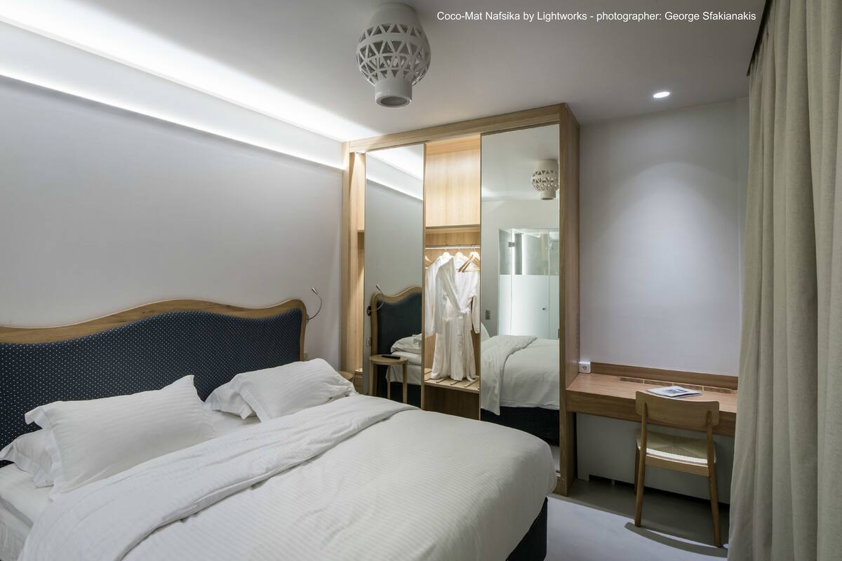 A modern hotel room with a large bed, a wooden desk, and a mirror.